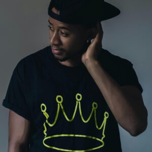 Portrait of a fashionable young man in a studio with a crown design on his shirt, exuding confidence.